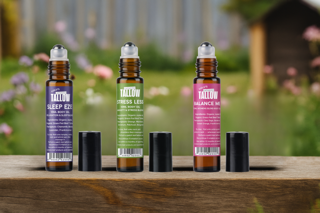 Three Lulu’s Untainted Tallow roll-on body oils—Sleep Eze, Stress Less, and Balance Me—displayed on a wooden surface with a blurred garden background